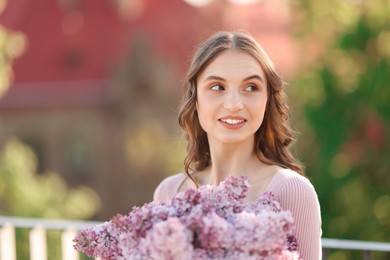 Photo of Smiling woman with bouquet of lilac flowers outdoors in morning