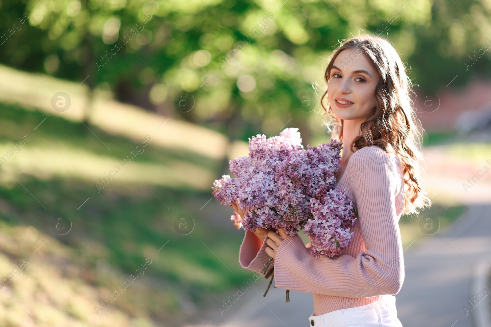 Smiling woman with bouquet of lilac flowers outdoors in morning. Space for text Photo of Smiling woman with bouquet of lilac flowers outdoors in morning. Space for text