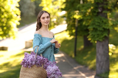 Photo of Smiling woman with bag of lilac flowers outdoors in morning. Space for text