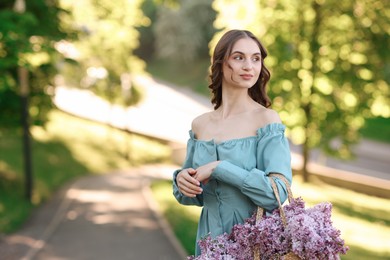 Photo of Beautiful woman with bag of lilac flowers outdoors in morning. Space for text
