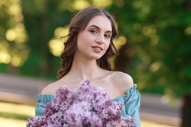 Photo of Portrait of smiling woman with bouquet of lilac flowers outdoors in morning