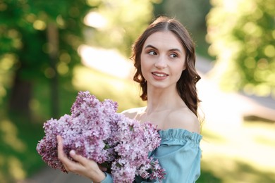 Photo of Smiling woman with bouquet of lilac flowers outdoors in morning