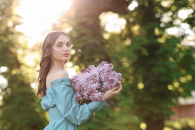 Photo of Beautiful woman with bouquet of lilac flowers outdoors in morning. Space for text