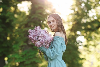 Photo of Smiling woman with bouquet of lilac flowers outdoors in morning