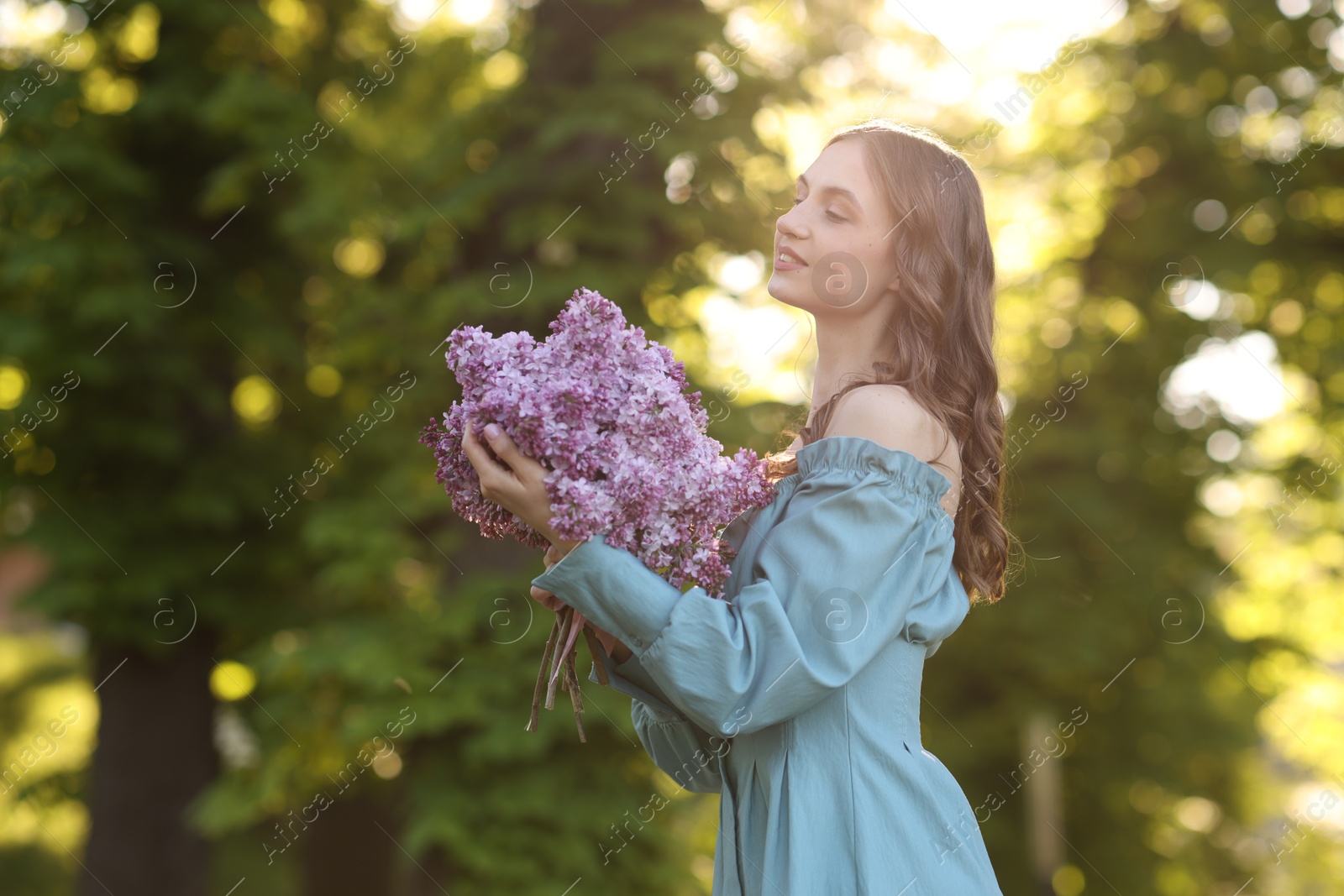 Smiling woman with bouquet of lilac flowers outdoors in morning. Space for text Photo of Smiling woman with bouquet of lilac flowers outdoors in morning. Space for text