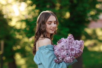 Photo of Smiling woman with bouquet of lilac flowers outdoors in morning