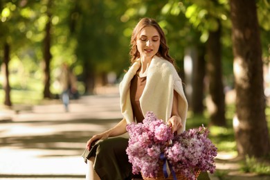 Photo of Smiling woman with basket of lilac flowers sitting on bench outdoors in morning. Space for text