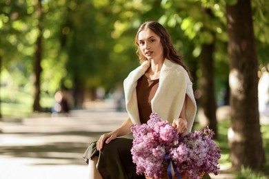 Photo of Beautiful woman with basket of lilac flowers sitting on bench outdoors in morning. Space for text