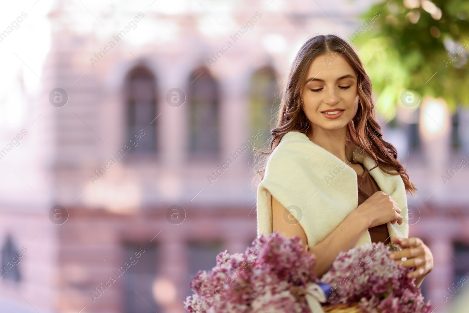 Smiling woman with basket of lilac flowers outdoors. Space for text Photo of Smiling woman with basket of lilac flowers outdoors. Space for text