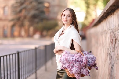 Photo of Smiling woman with basket of lilac flowers on city street