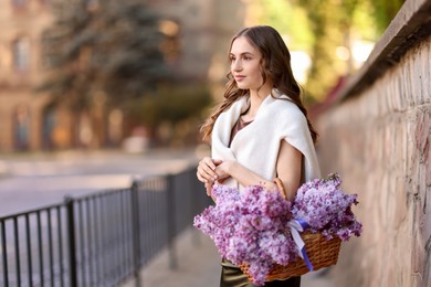 Photo of Beautiful woman with basket of lilac flowers on city street