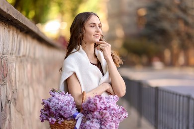 Photo of Smiling woman with basket of lilac flowers on city street