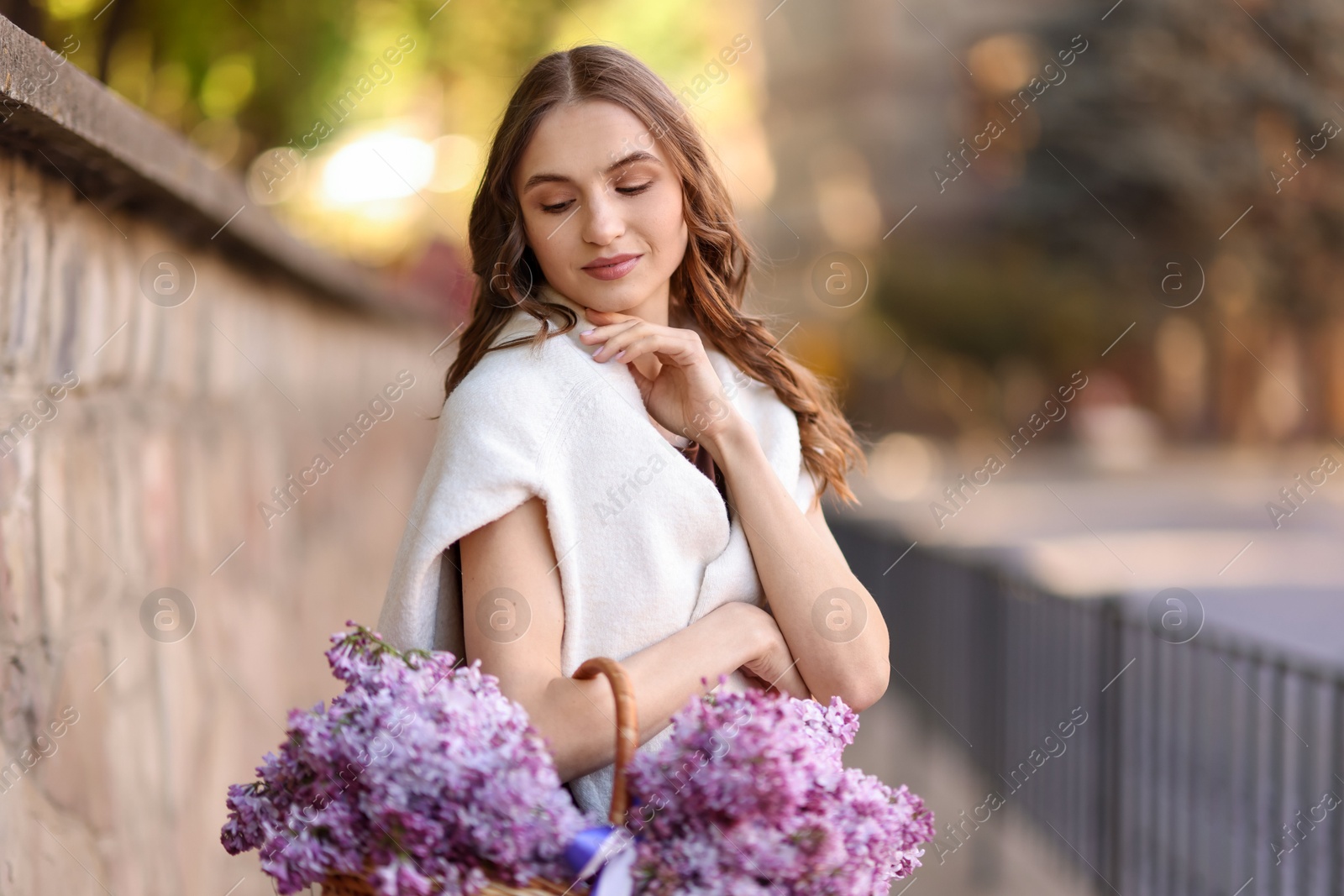 Beautiful woman with basket of lilac flowers on city street Photo of Beautiful woman with basket of lilac flowers on city street