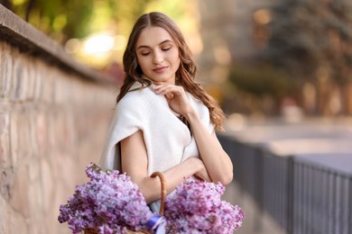 Photo of Beautiful woman with basket of lilac flowers on city street