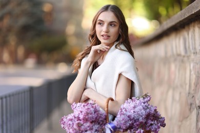 Photo of Beautiful woman with basket of lilac flowers on city street