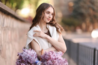 Photo of Beautiful woman with basket of lilac flowers on city street