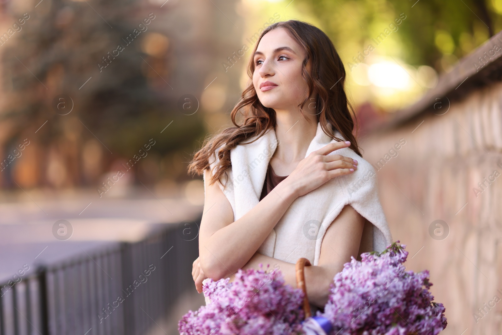 Beautiful woman with basket of lilac flowers on city street Photo of Beautiful woman with basket of lilac flowers on city street