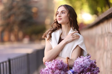 Photo of Beautiful woman with basket of lilac flowers on city street
