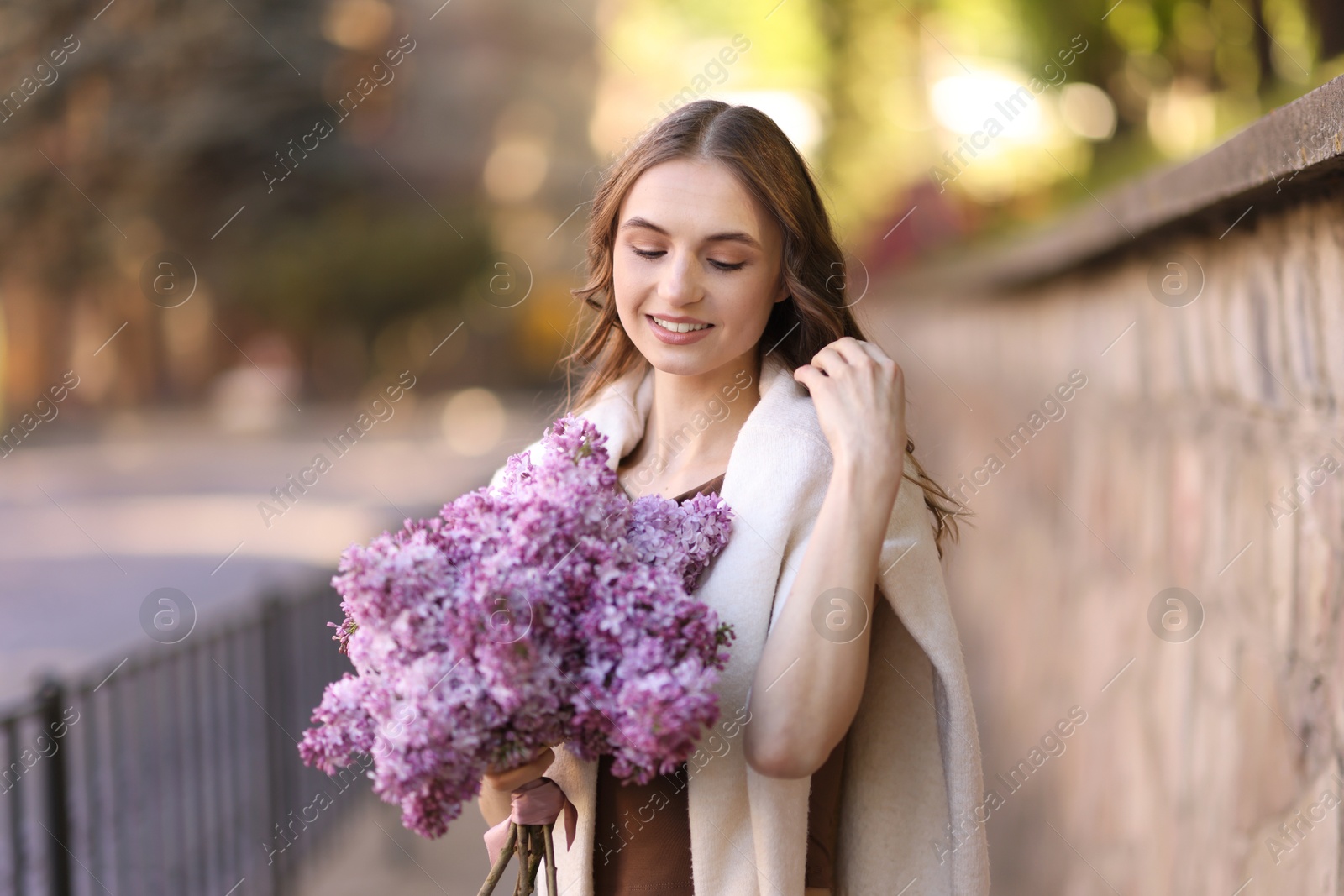 Smiling woman with bouquet of lilac flowers on city street Photo of Smiling woman with bouquet of lilac flowers on city street