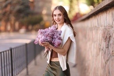 Photo of Smiling woman with bouquet of lilac flowers on city street