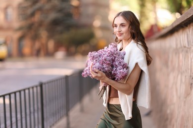 Photo of Beautiful woman with bouquet of lilac flowers on city street. Space for text