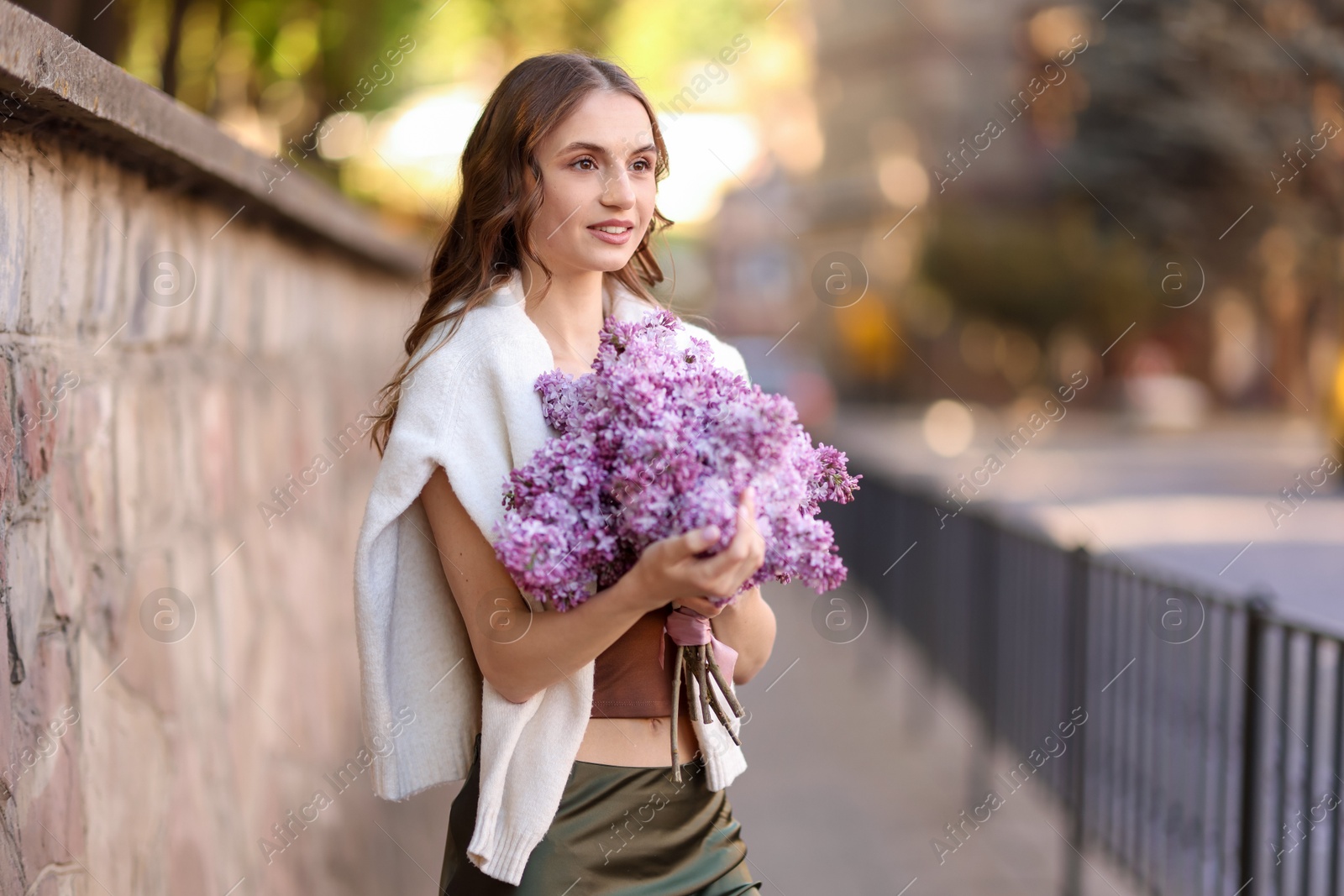 Smiling woman with bouquet of lilac flowers on city street Photo of Smiling woman with bouquet of lilac flowers on city street