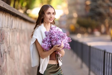 Photo of Smiling woman with bouquet of lilac flowers on city street