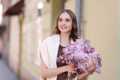 Photo of Smiling woman with bouquet of lilac flowers near building outdoors