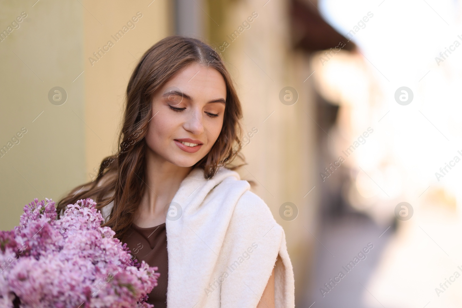 Smiling woman with bouquet of lilac flowers on blurred background. Space for text Photo of Smiling woman with bouquet of lilac flowers on blurred background. Space for text
