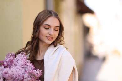 Photo of Smiling woman with bouquet of lilac flowers on blurred background. Space for text
