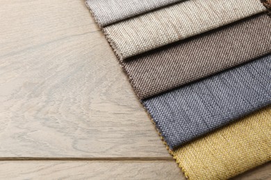 Photo of Samples of different fabrics on wooden table, closeup. Space for text