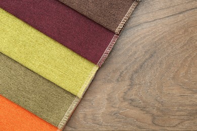 Photo of Samples of different fabrics on wooden table, top view. Space for text