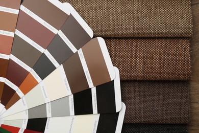 Photo of Samples of different fabrics and color selection chart on wooden table, closeup