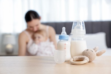 Photo of Mother with her little baby indoors, focus on bottles of milk and teether