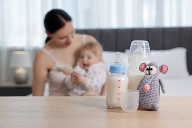 Photo of Mother with her little baby indoors, focus on bottles of milk and toy