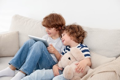 Photo of Cute little brothers with tablet on sofa at home