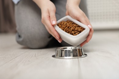 Photo of Woman putting dry pet food into bowl on floor at home, closeup