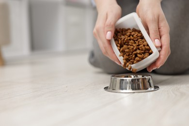 Photo of Woman putting dry pet food into bowl on floor at home, closeup. Space for text