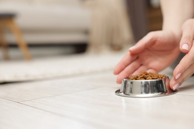 Photo of Woman with bowl of dry pet food on floor at home, closeup. Space for text