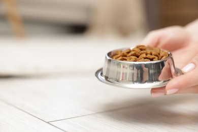 Photo of Woman with bowl of dry pet food on floor at home, closeup. Space for text