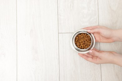Photo of Woman with bowl of dry pet food on floor at home, top view. Space for text