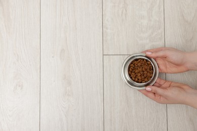 Photo of Woman with bowl of dry pet food on floor at home, top view. Space for text