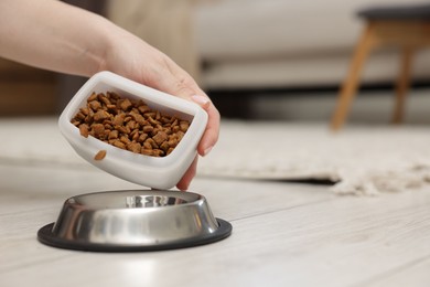 Photo of Woman putting dry pet food into bowl on floor at home, closeup. Space for text