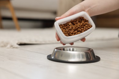 Photo of Woman putting dry pet food into bowl on floor at home, closeup. Space for text