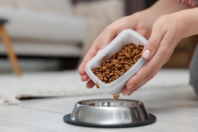 Photo of Woman putting dry pet food into bowl on floor at home, closeup. Space for text