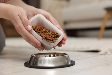 Photo of Woman putting dry pet food into bowl on floor at home, closeup. Space for text