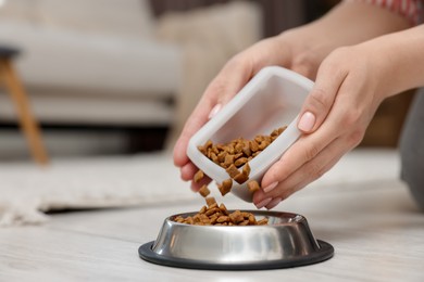 Photo of Woman putting dry pet food into bowl on floor at home, closeup