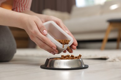 Photo of Woman putting dry pet food into bowl on floor at home, closeup