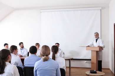 Photo of Senior doctor giving lecture in conference room with projection screen