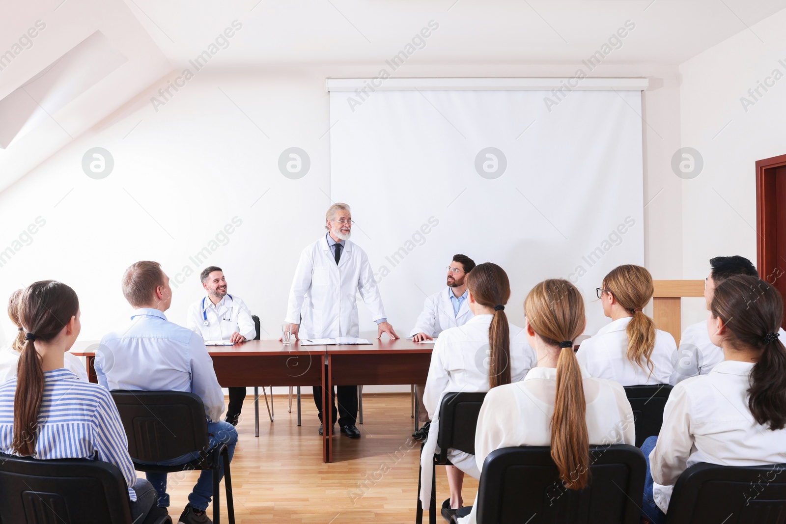 Senior doctor giving lecture near projection screen in conference room Photo of Senior doctor giving lecture near projection screen in conference room